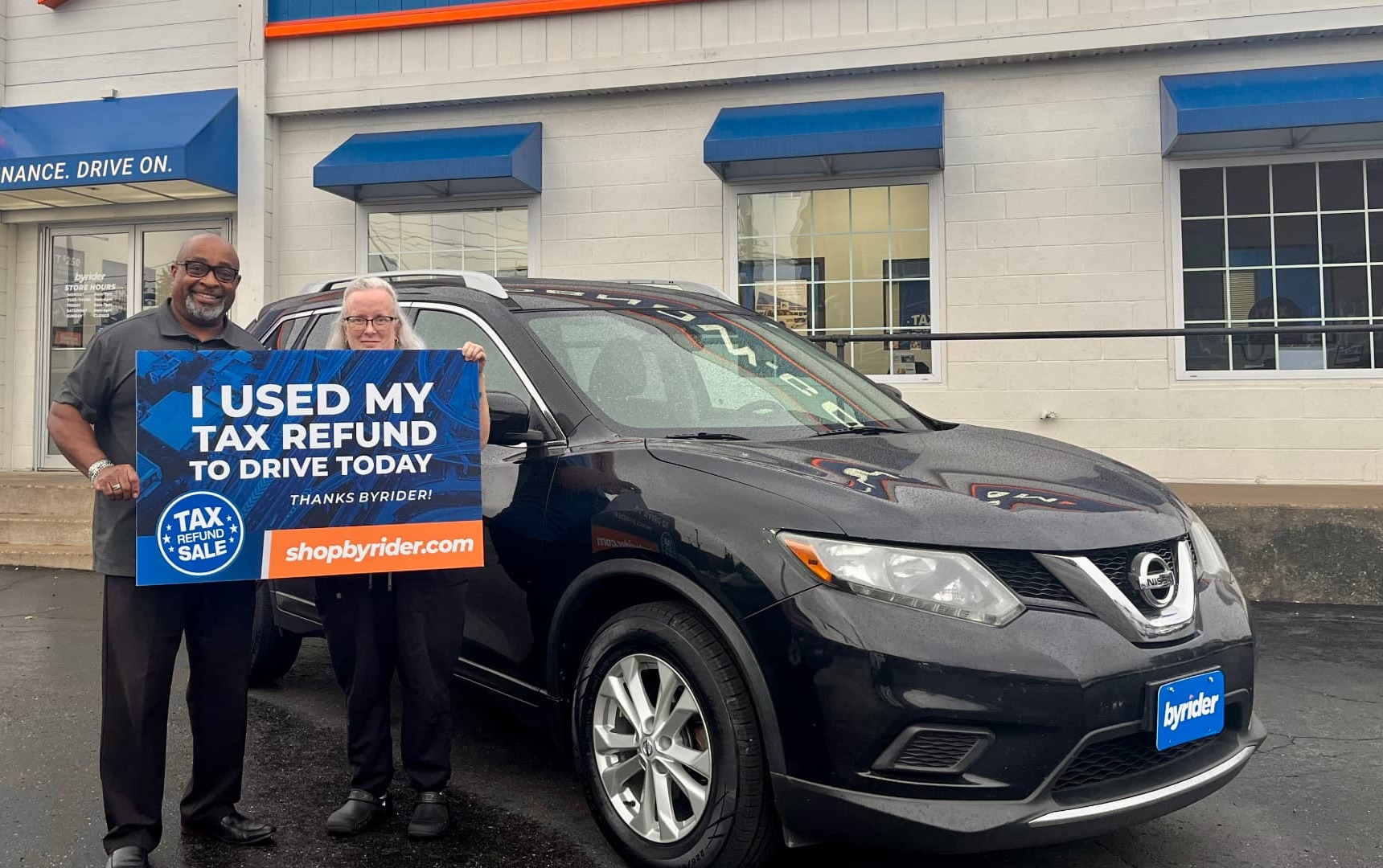 Byrider customers holding an I Used My Tax Refund to Drive Today sign next to their Nissan Rogue during the Tax Refund Sale in Ohio