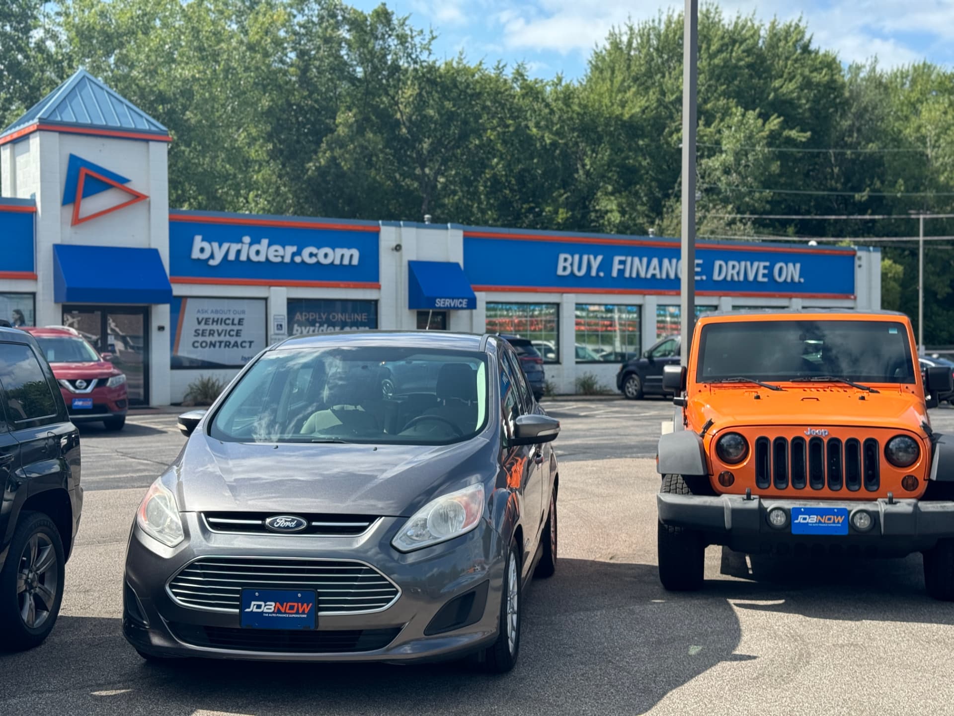 Byrider Amherst used car dealership storefront at 7550 Leavitt Rd, Amherst, Ohio, with a Ford C-Max and orange Jeep Wrangler on the lot